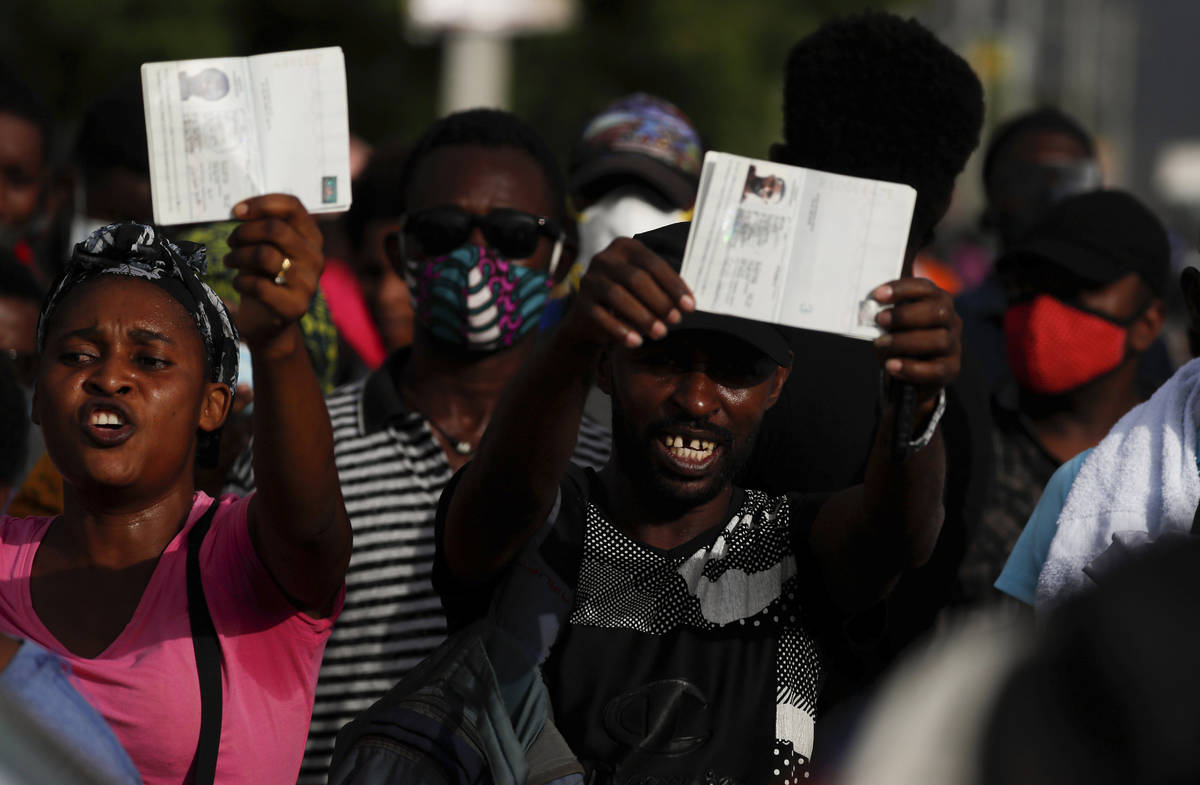 Haitians wave their passports shouting "Help, refugee," as they gather outside the U. ...