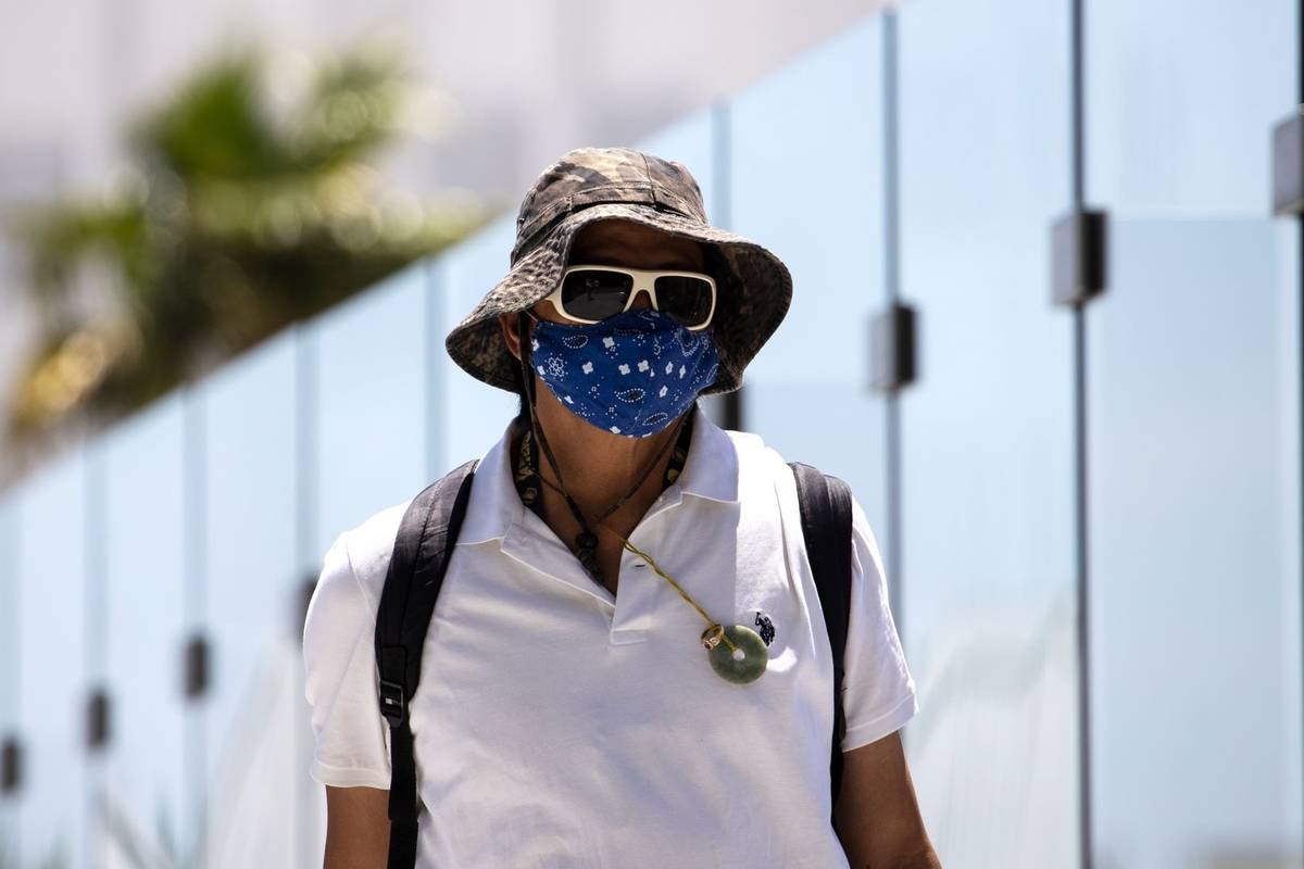 A pedestrian wears a large hat to protect himself from sun as he crosses the pedestrian bridge ...