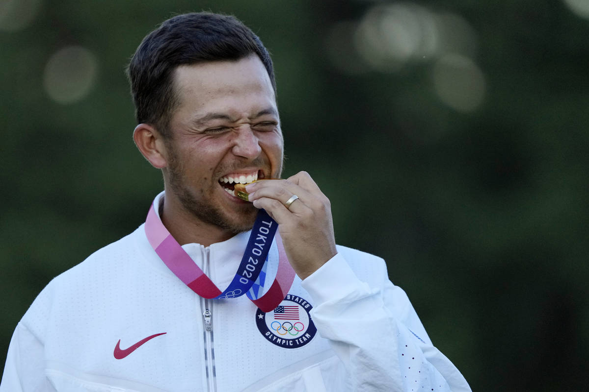 Xander Schauffele, of the United States, walks bites his gold medal in the men's golf at the 20 ...