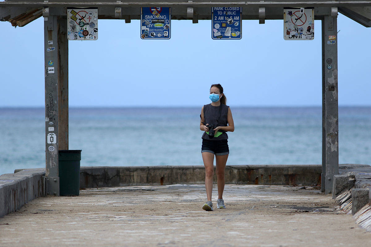 A woman wears a mask as she walks along a closed Waikiki Beach pier in Honolulu in March 2020. ...