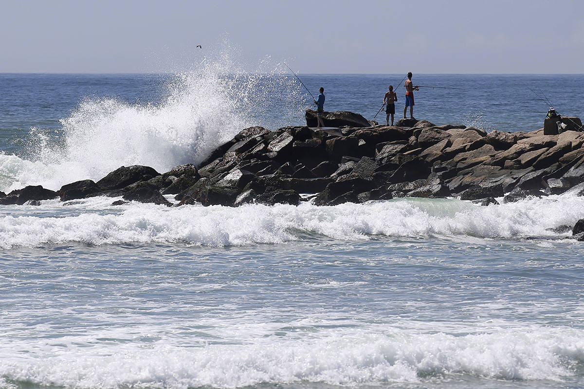 People fish as large waves hit the rocks at the Charlestown Breachway Saturday, Aug. 21, 2021, ...
