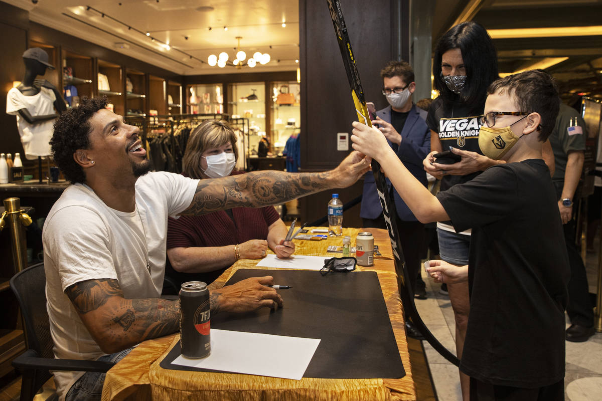 Former Golden Knights player Ryan Reaves, left, signs a hockey stick for Gus Karris, 8, during ...