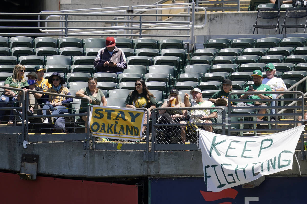 Fans sit behind a sign that reads Stay in Oakland during the first inning of a baseball game be ...