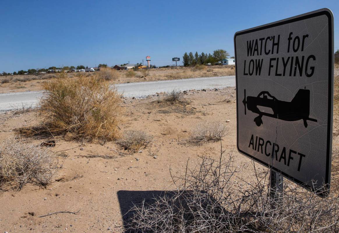 The sign warning residents to watch for low flying aircraft is shown near unpaved airstrip, on ...