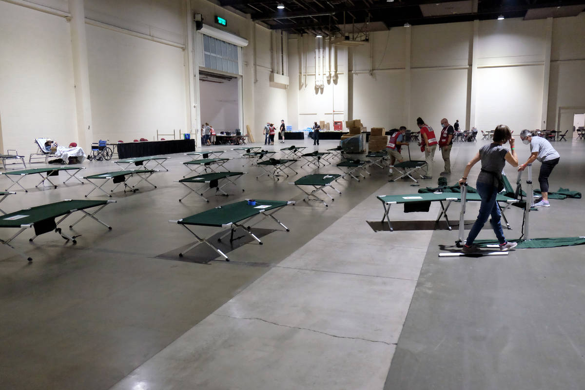 Red Cross workers and volunteers set up cots at an evacuation facility for people displaced by ...
