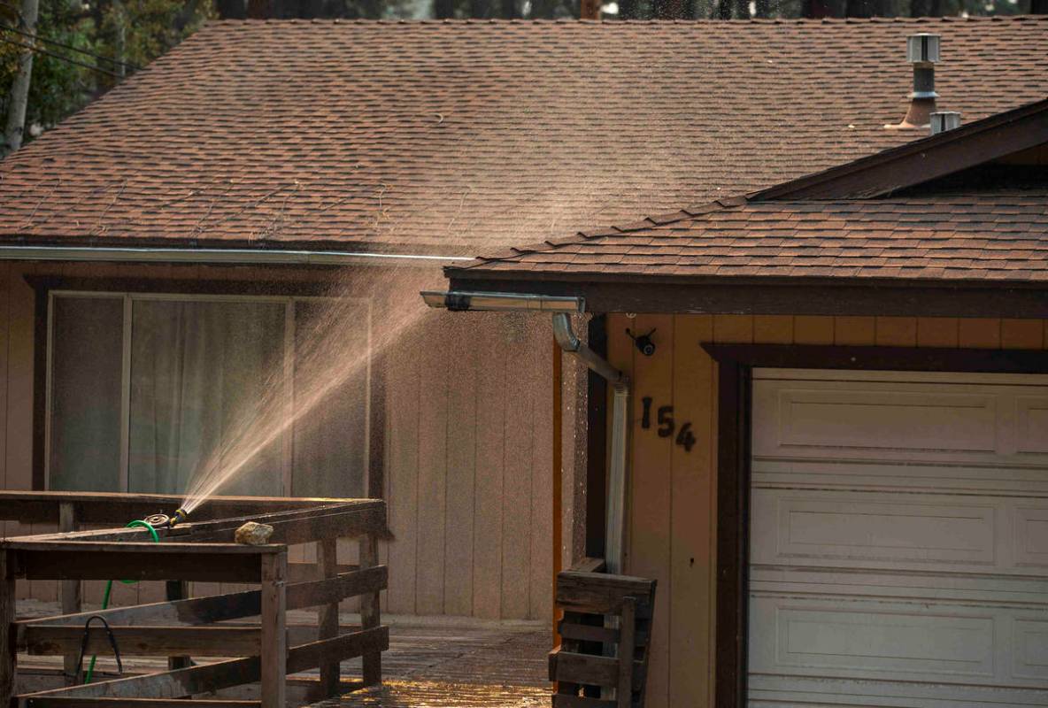 A sprinkler douses of evacuated home from the Caldor Fire on Wednesday, Sept. 1, 2021, in Kings ...