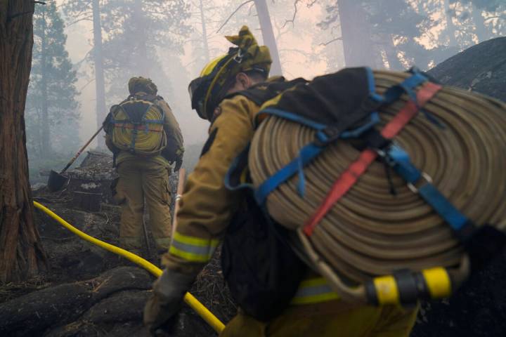 Two firefighters from Cosumnes Fire Department carry water hoses while holding a fire line to k ...