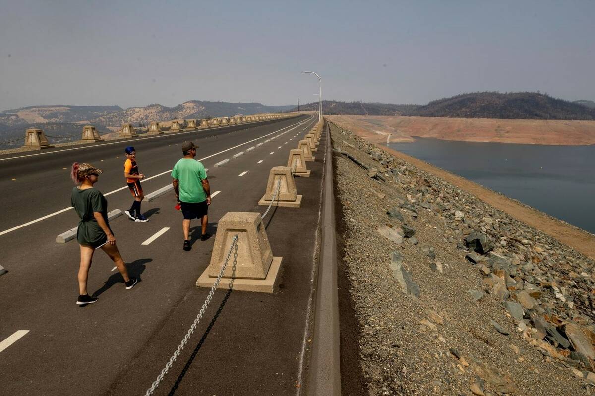 Pedestrians walk across Oroville Dam at Lake Oroville State Recreation Area as drought conditio ...