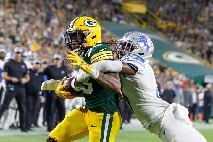 Green Bay Packers running back Aaron Jones, left, scores a touchdown as he is tackled by Detroi ...