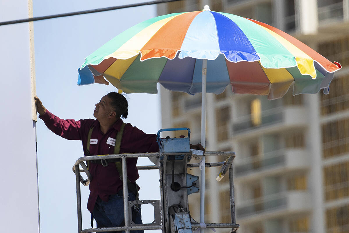 A worker uses a giant umbrella to protect himself from sun as he works on an outdoor advertisin ...