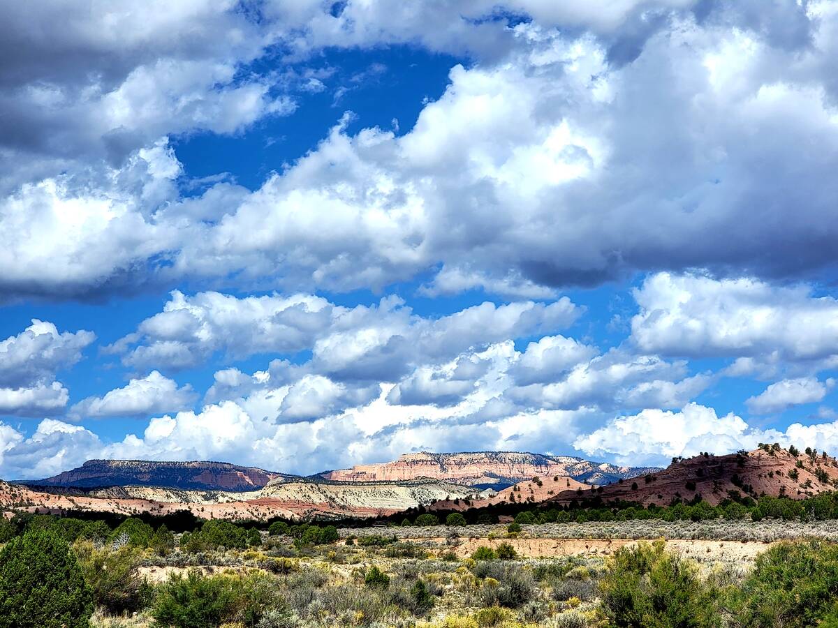 Bountiful clouds drift in the big skies above a collection of mesas, canyons, buttes, spires an ...