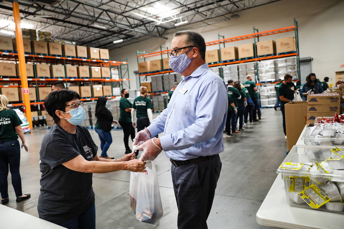 Brian Burton, president and CEO of Three Square Food Bank, hands a packed bag of food to volunt ...
