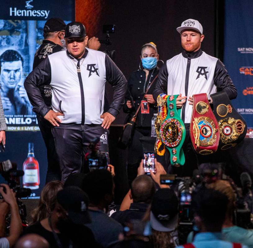 Boxer Canelo Alvarez holds his belts with trainer Eddy Reynoso standing before media members du ...