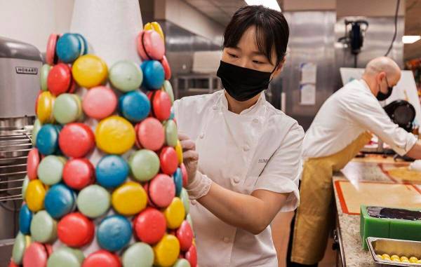 Assistant executive pastry chef Sunny Lee, left, uses icing to apply macaroons to a decorative ...