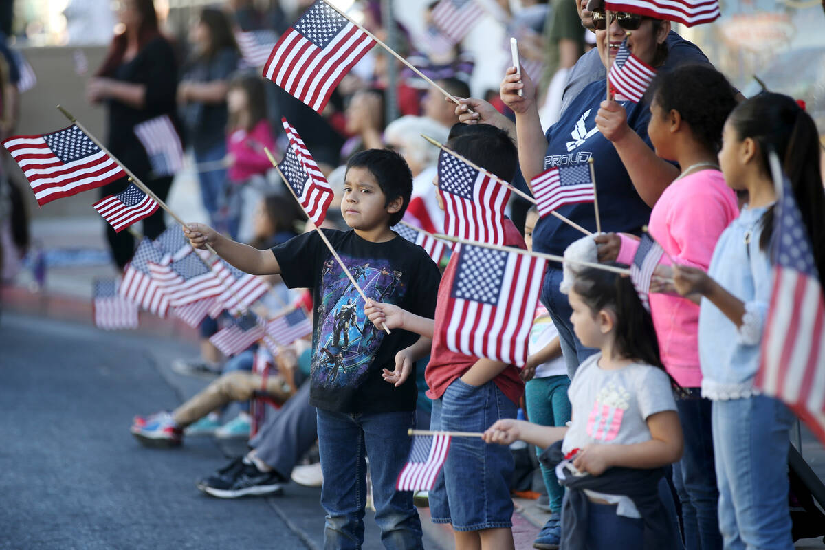 Spectators, including Nick Camocho, 9, left, wave American flags during the Veterans Day Parade ...