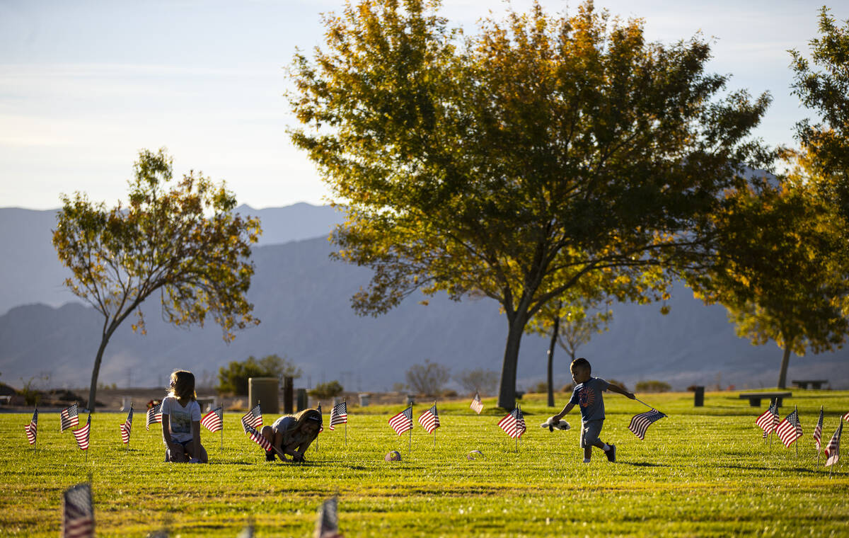 Enoch Ayala, 2, of Boulder City, runs with a flag as volunteers place American flags on graves ...