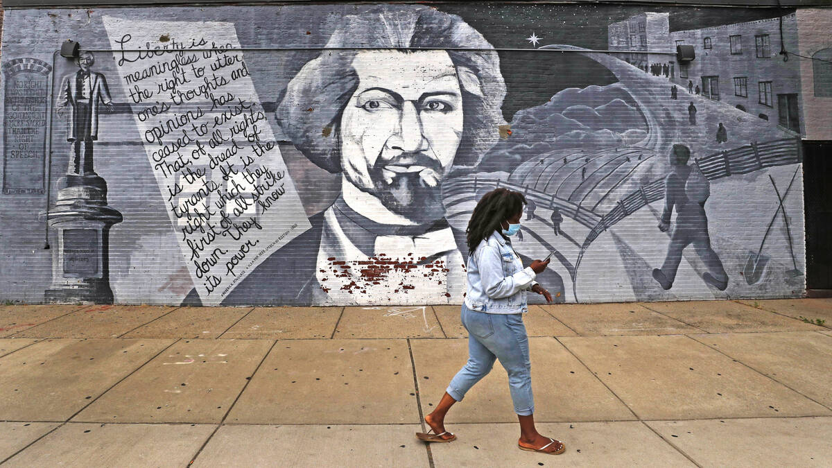 In this Wednesday, June 24, 2020, photograph, a woman walks past a mural in tribute to Frederic ...