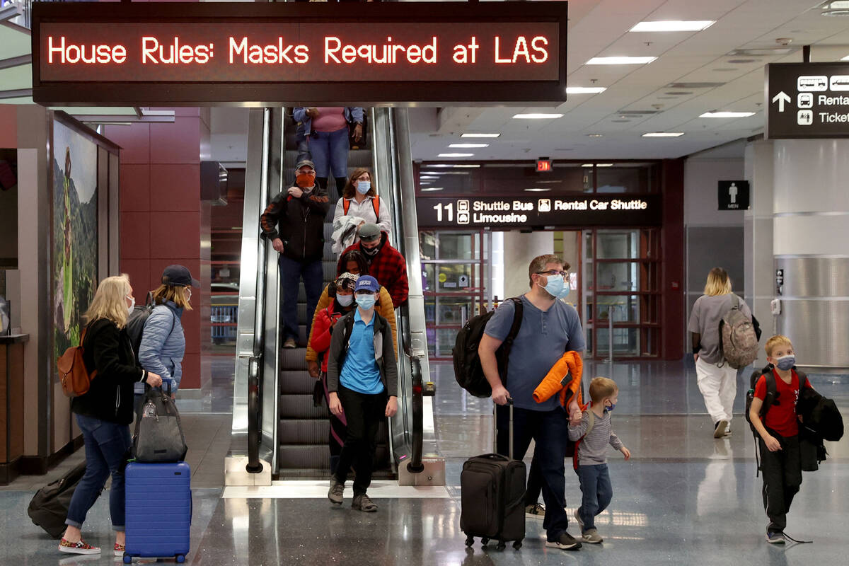 Masked travelers walk through Terminal 1 at McCarran International Airport in Las Vegas Friday, ...