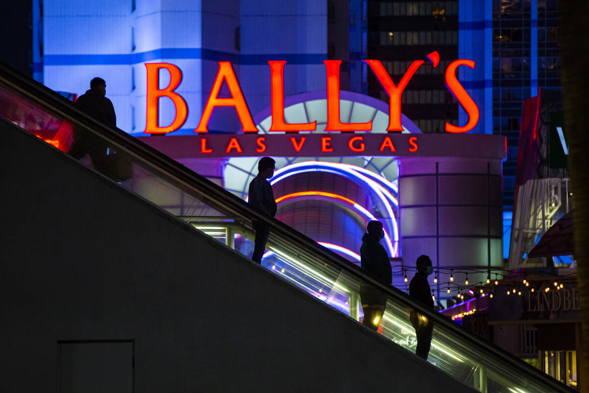 People are silhouetted by a sign for Bally's as they descend an escalator from a pedestrian bri ...