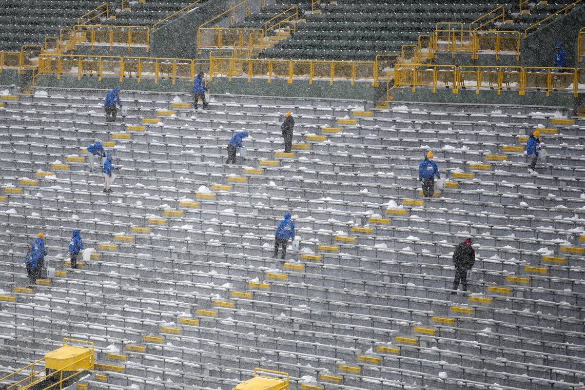 Workers put salt in the seating bowl at Lambeau Field before an NFL football game between the G ...