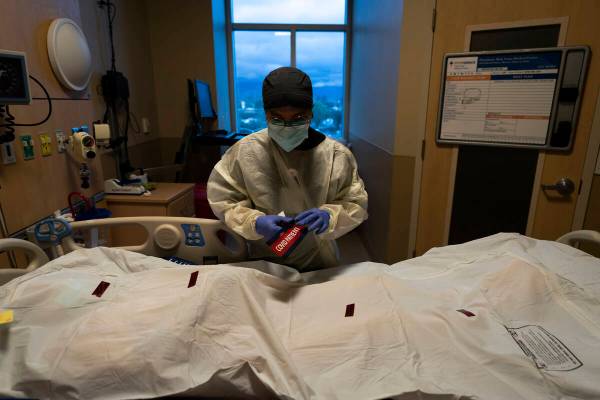 Registered nurse Bryan Hofilena attaches a "COVID Patient" sticker on a body bag of a ...