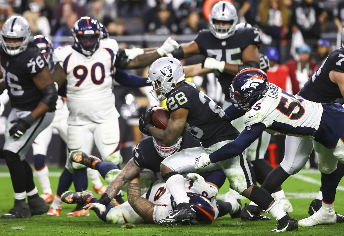 Raiders running back Josh Jacobs (28) runs the ball under pressure from Denver Broncos outside ...