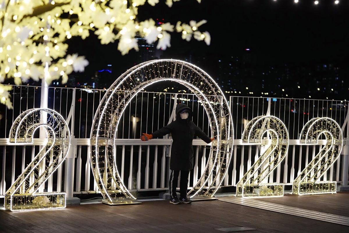 A visitor wearing a face mask poses for a photo in front of an illuminated decorations on New Y ...