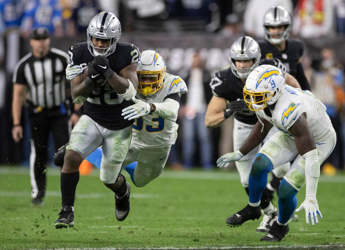 Raiders running back Josh Jacobs (28) leaps through a hole past Los Angeles Chargers free safet ...