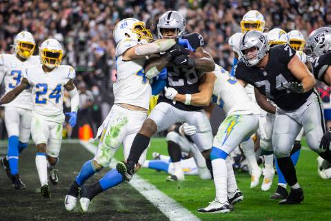 Raiders running back Josh Jacobs (28) runs for a touchdown under pressure from Los Angeles Char ...