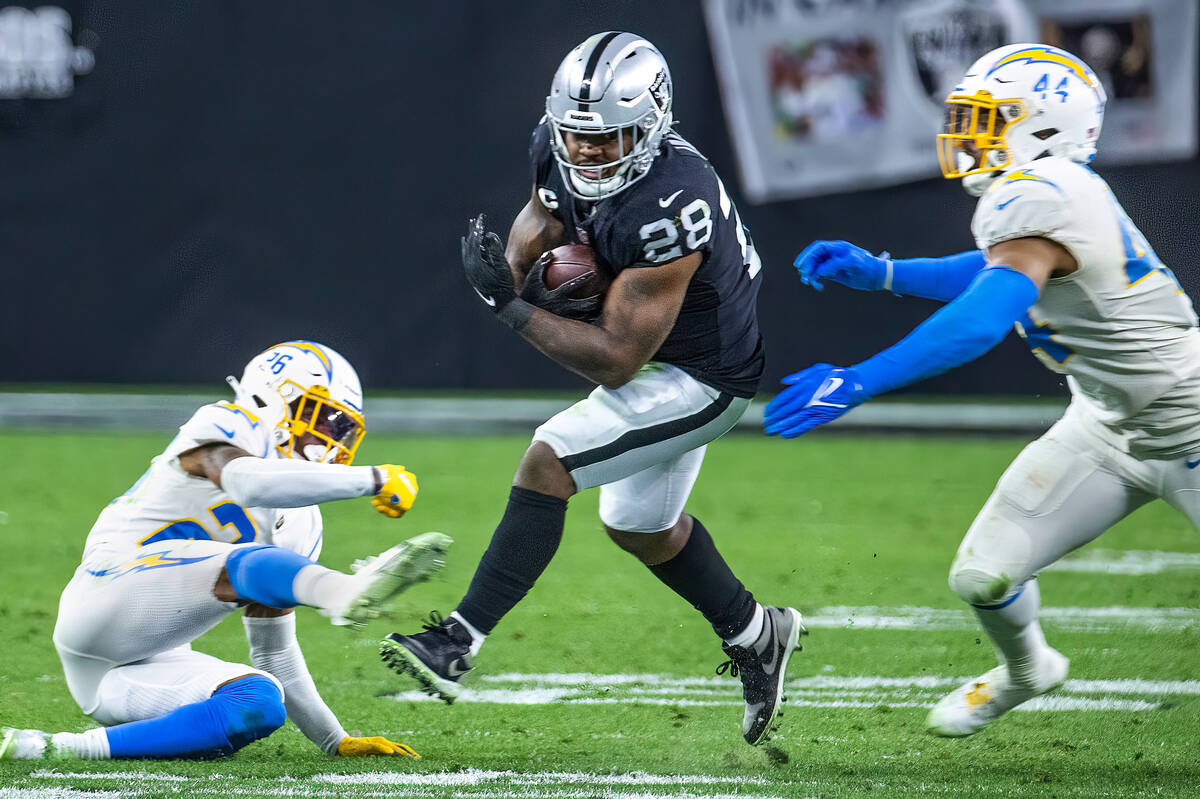 Raiders running back Josh Jacobs (28) looks to drive between Los Angeles Chargers cornerback As ...