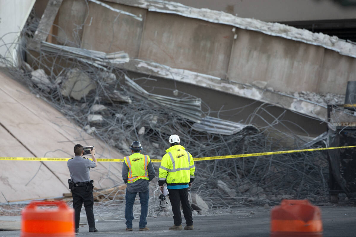 A Las Vegas police officer and Las Vegas Paving Corp. employees survey the damage after a porti ...