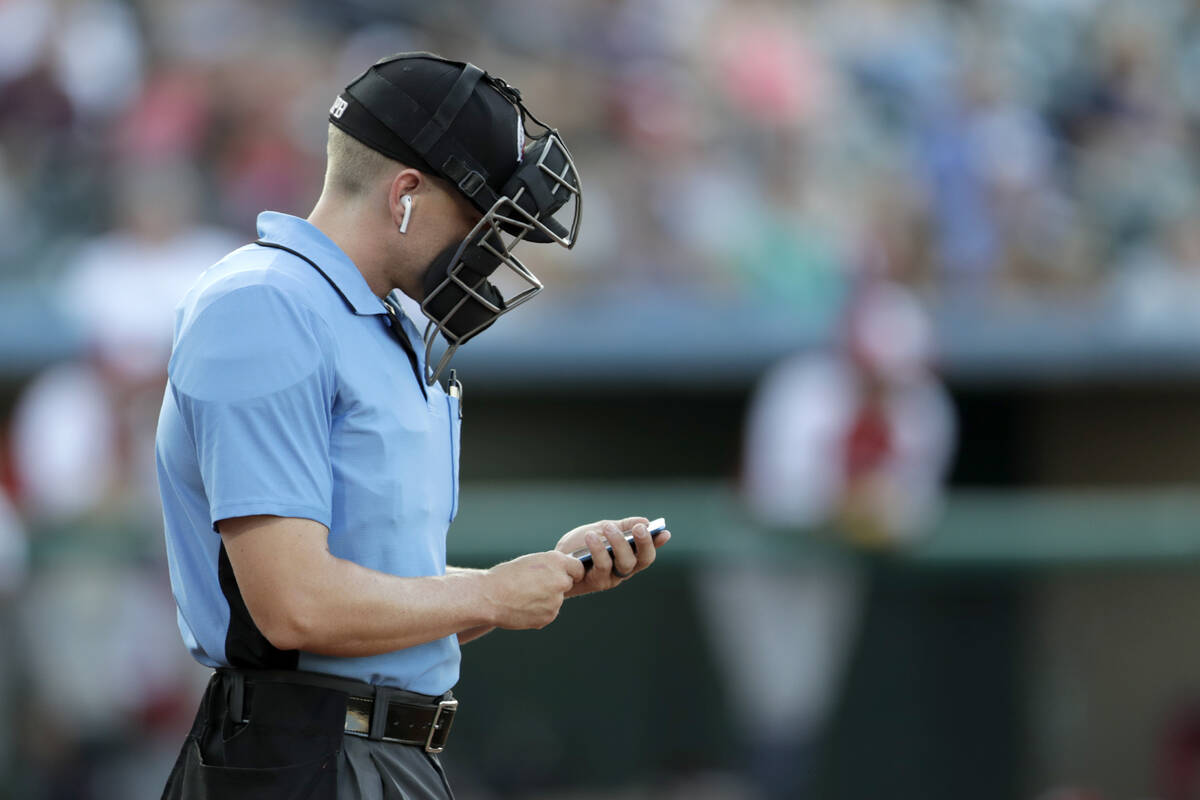 Home plate umpire Brian deBrauwere checks an iPhone while wearing an earpiece prior to the star ...