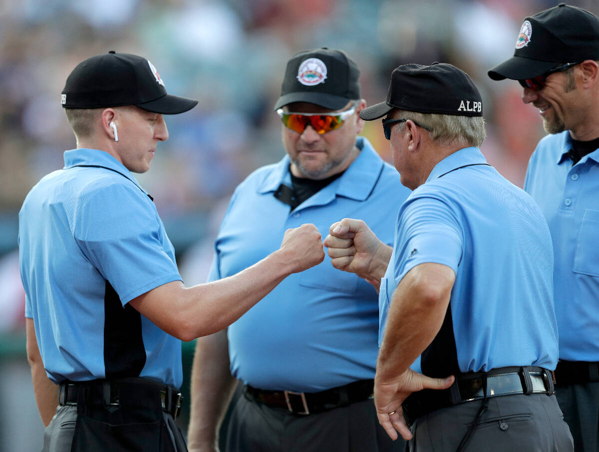 Home plate umpire Brian deBrauwere, left, huddles with officials while wearing an earpiece conn ...