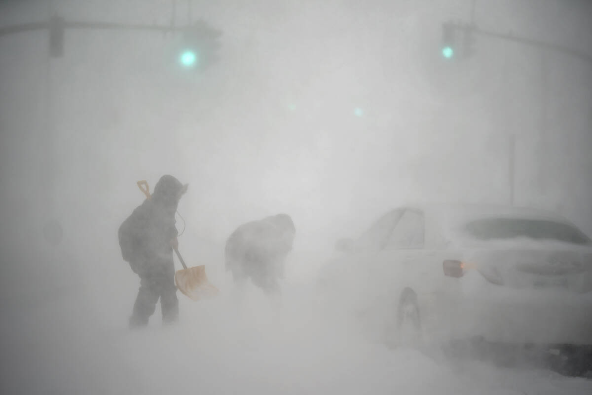 A stranded motorist, at right, gets help shoveling out their car from a passerby with a shovel ...