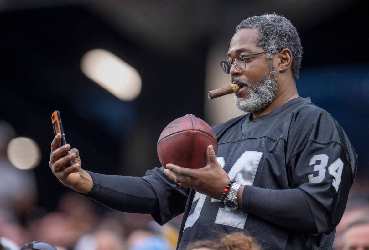 A fan shoots a game ball tossed into the stands by a player after a score during the first half ...