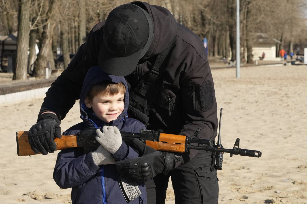 A member of a Ukrainian far-right group helps a boy to hold a Kalashnikov assault rifle during ...