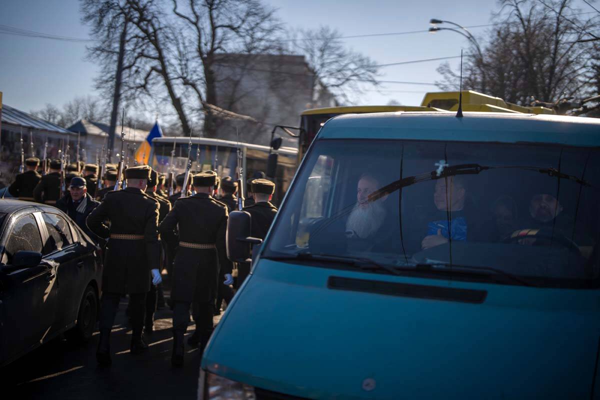 Honor guard soldiers walk past a van carrying priests in the city of Kyiv, Ukraine, Tuesday, Fe ...