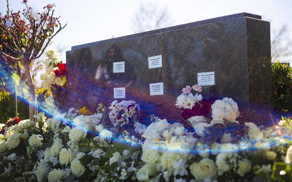 Mourners are reflected in the headstone at the burial site of the five Zacarias family members ...