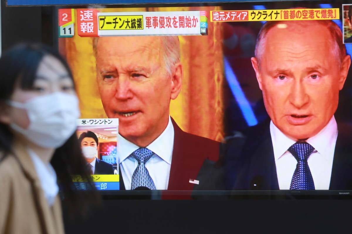 A woman walks past a TV screen showing images of Russia's President Vladimir Putin and U.S. Pre ...