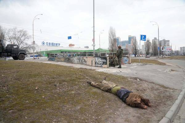A body of killed soldier lies on the ground as Ukrainian Army soldiers sit next in Kyiv, Ukrain ...