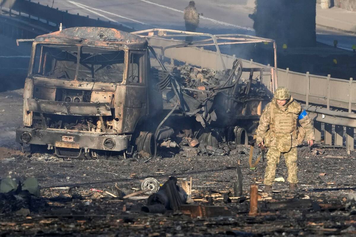 A Ukrainian soldier walks past debris of a burning military truck, on a street in Kyiv, Ukraine ...