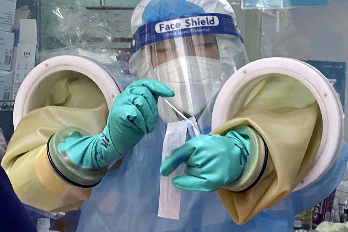 FILE - A worker handles a coronavirus test sample at a private testing site in Beijing, Wednesd ...