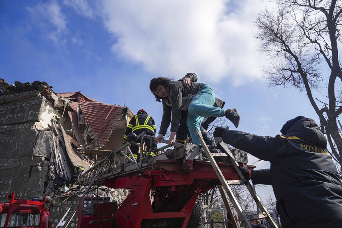 Firefighters help a woman to evacuate from a damaged by shelling apartment building in Mariupol ...