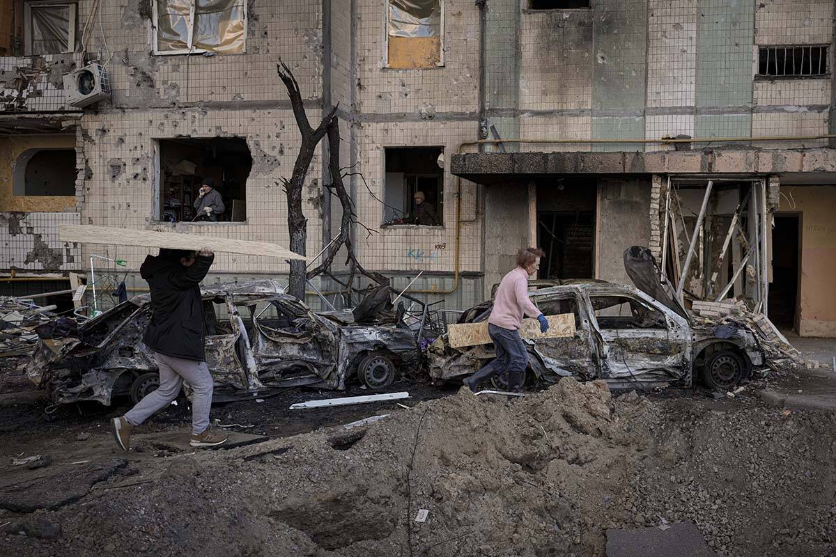 People carry wooden boards to cover the windows of a building damaged by a bombing the previous ...