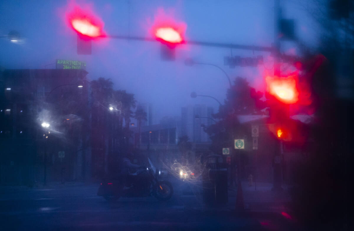 A motorcyclist drives along Fremont Street as pictured through raindrops on a window on Monday, ...