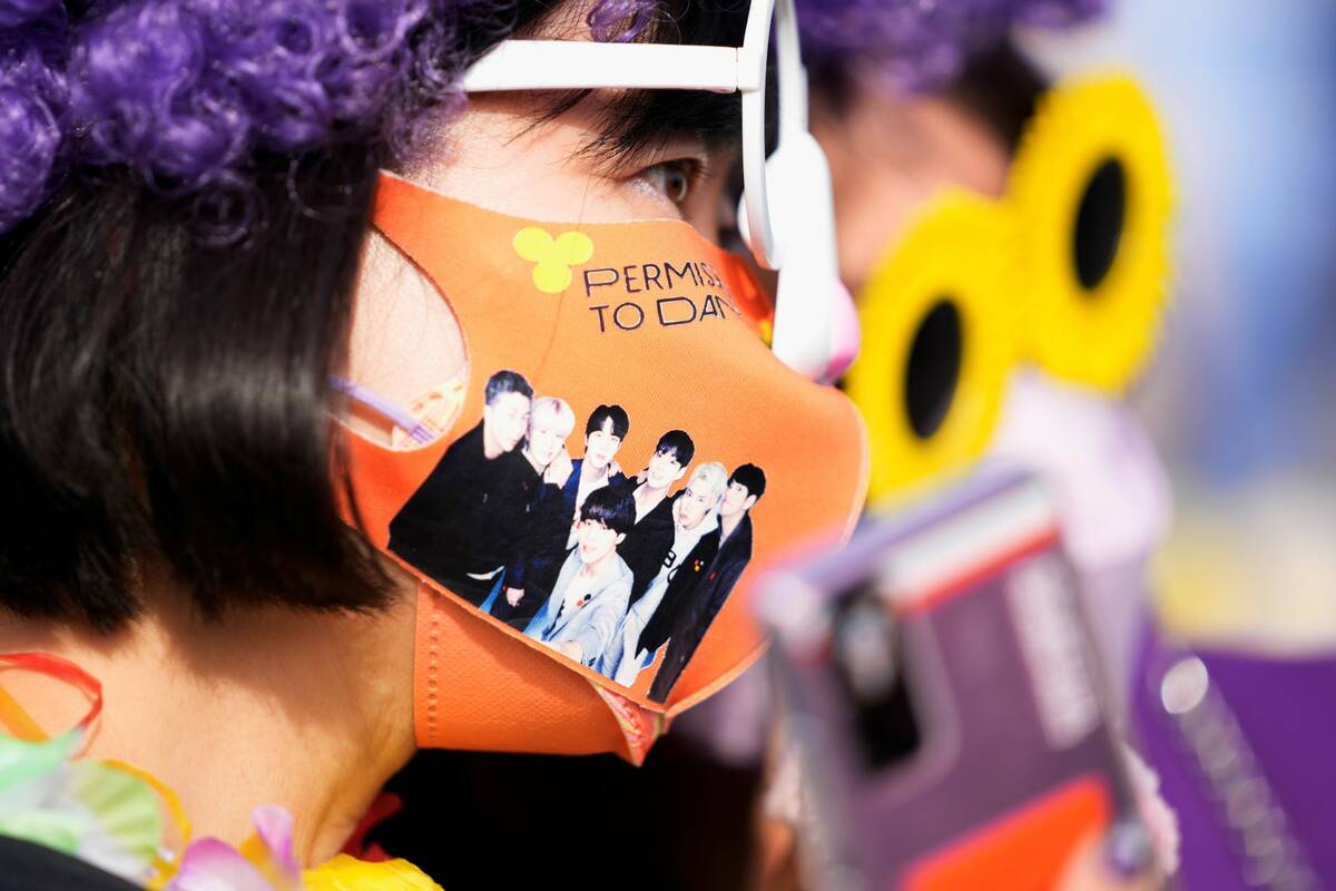 A fan of South Korean K-pop band BTS wears a face mask with a photo of BTS upon their arrival f ...