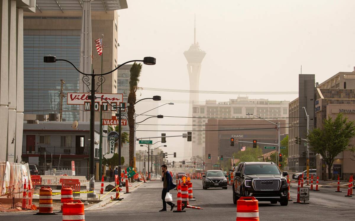 A pedestrian crosses Las Vegas Boulevard in downtown as winds bring in a dust storm on Monday, ...