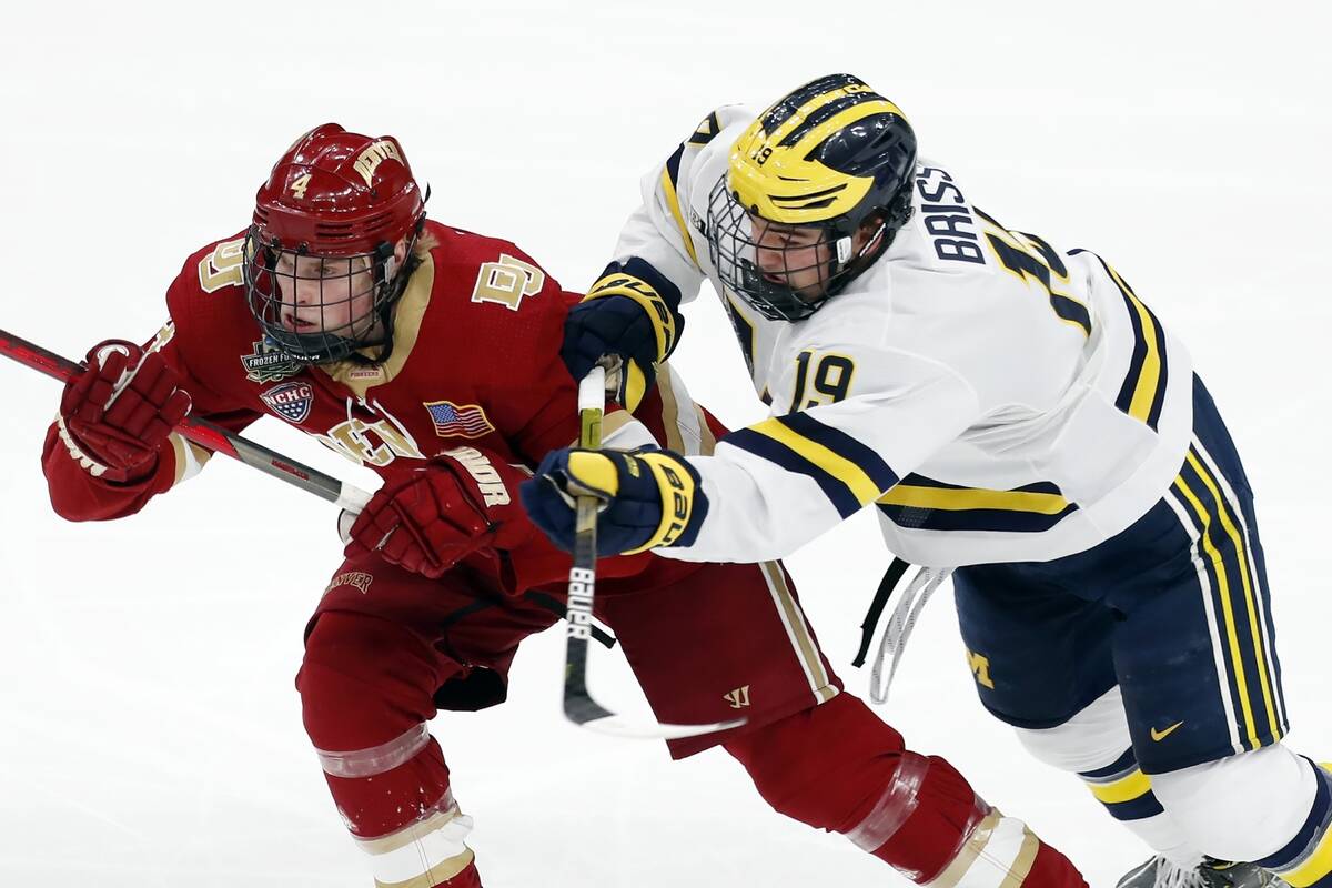 Michigan's Brendan Brisson (19) checks Denver's Jack Devine (4) during the first period of an N ...