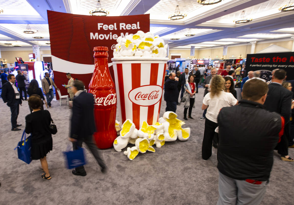 Attendees walk by a display at the Coca-Cola booth at the CinemaCon trade show at Caesars Palac ...
