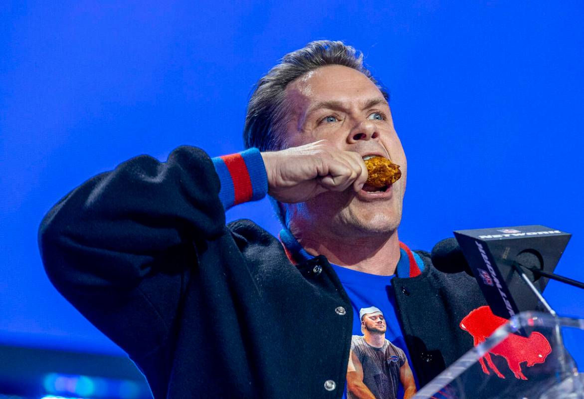 Kyle Brandt bites a chicken wing as he announces a Buffalo Bills selection at the Draft Theater ...